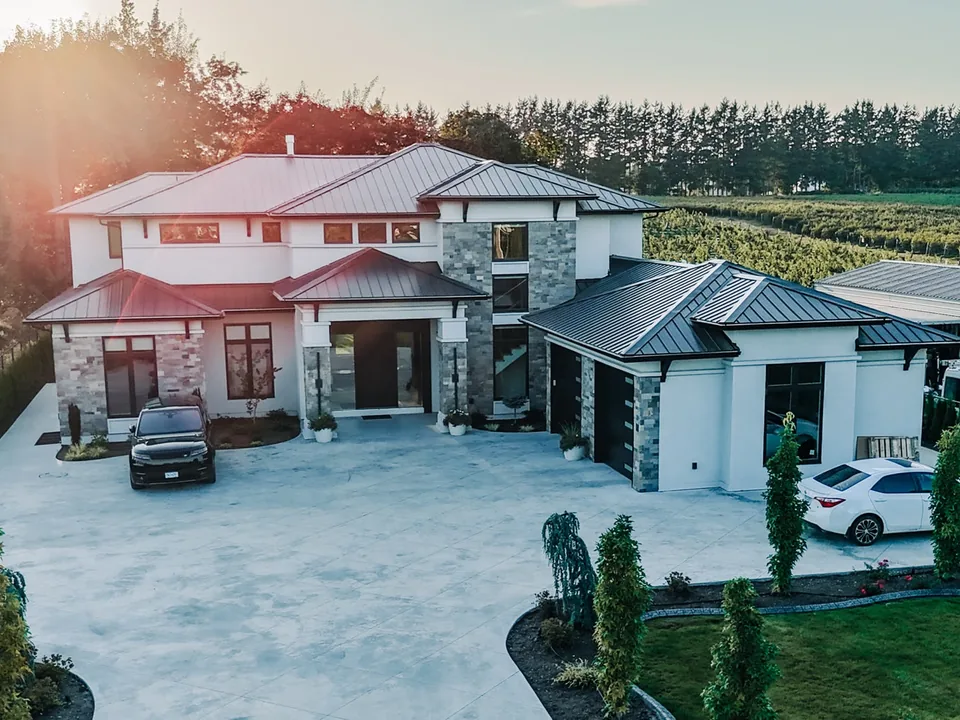 Aerial view of the completed custom farm home at sunset, with a wide concrete driveway and landscaped grounds