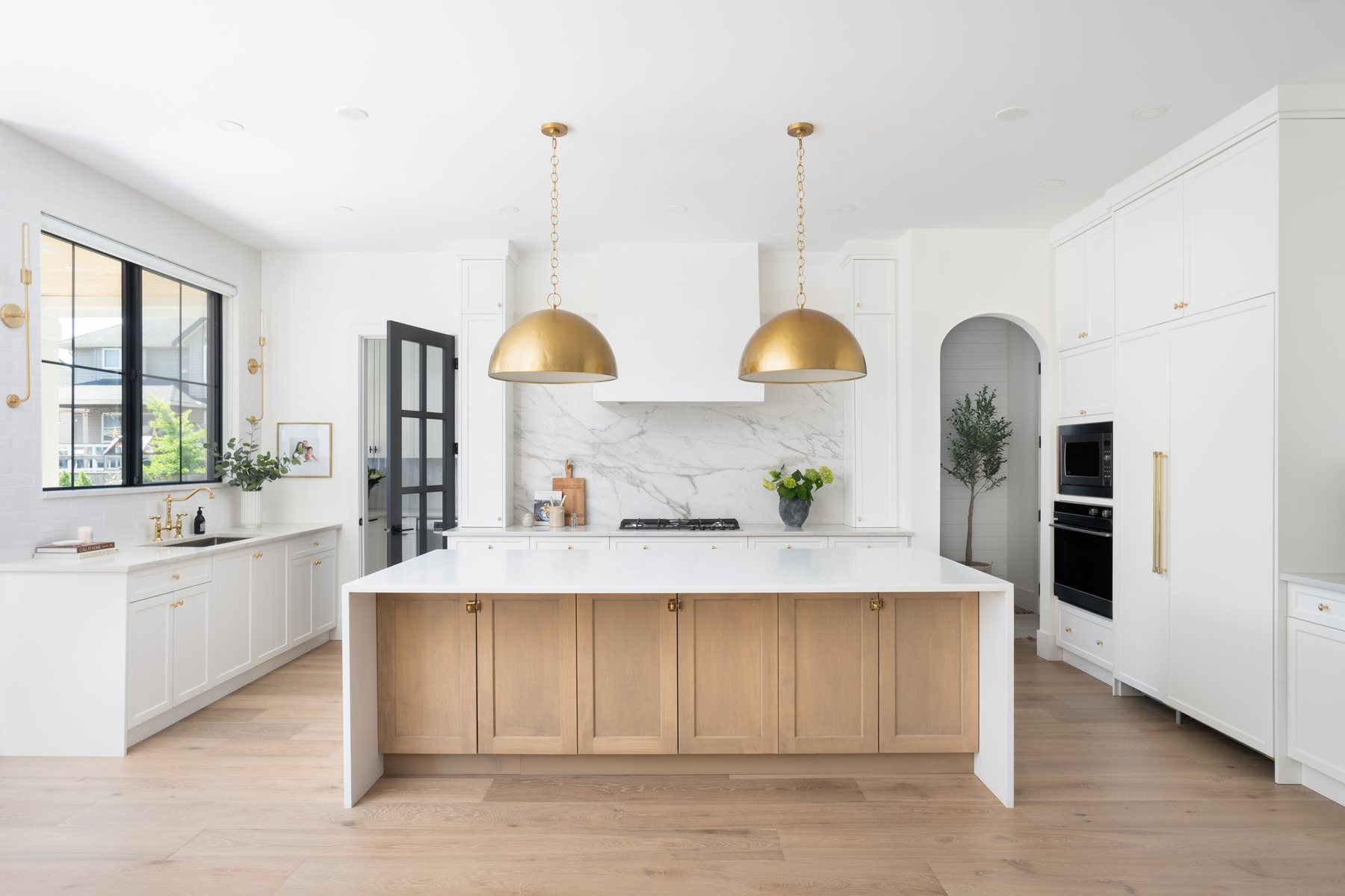 Bright custom kitchen with white cabinetry, an oak island, and brass pendant lights