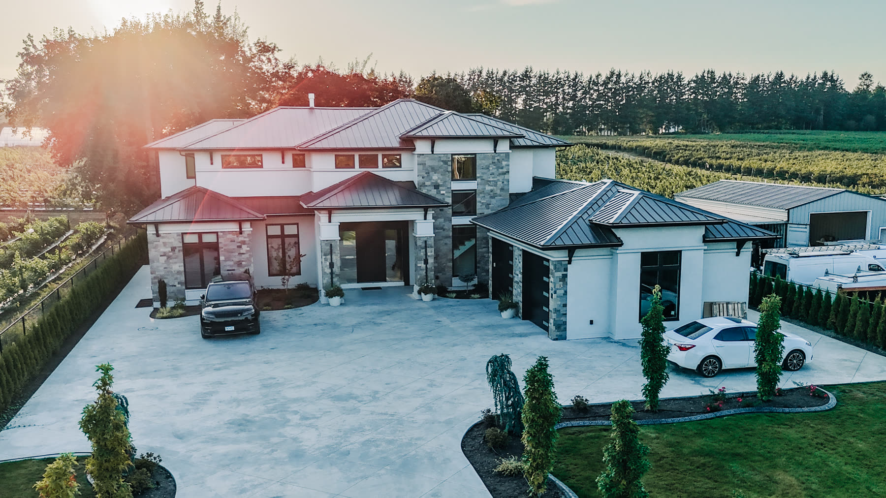 Aerial view of the completed custom farm home at sunset, with a wide concrete driveway and landscaped grounds